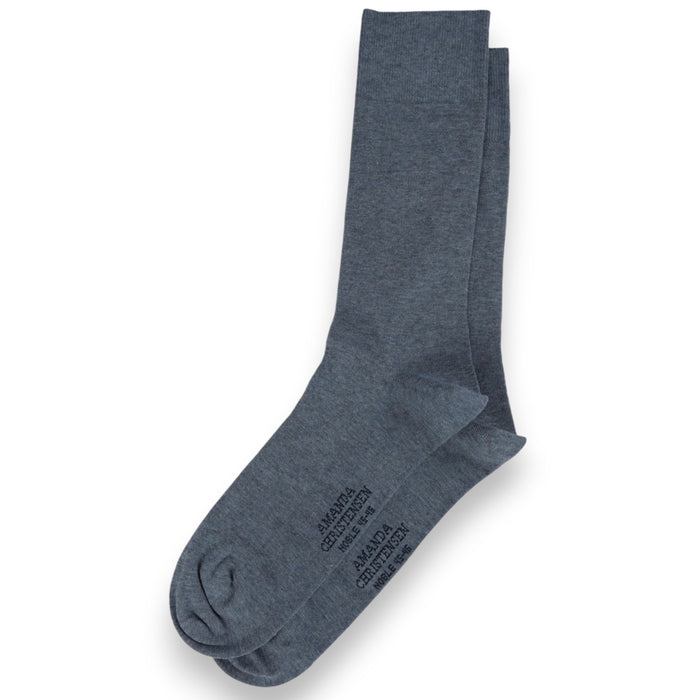 A pair of denim blue, mid-calf socks from AMANDA CHRISTENSEN are laid flat on a white background, with subtle text printed on the sole—these NOBLE Cotton & Cashmere Blend socks embody understated elegance and comfort inspired by classic Scandinavian men’s accessories.