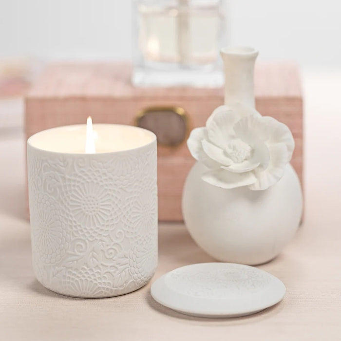 The CAMEO LONG NECK PORCELAIN BUD VASE by ZODAX is a round, white vase with a matte finish, featuring a narrow neck and a detailed floral embellishment on the front.