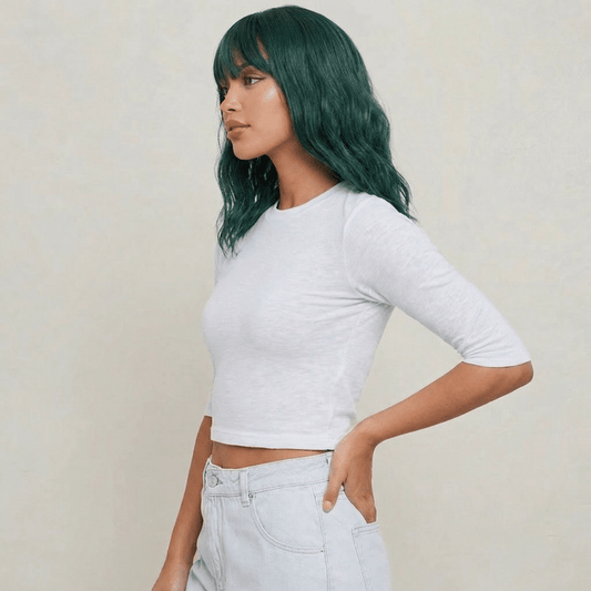 Short green wig with bangs worn by a model in a white crop top, showcasing wavy texture and vibrant emerald color.