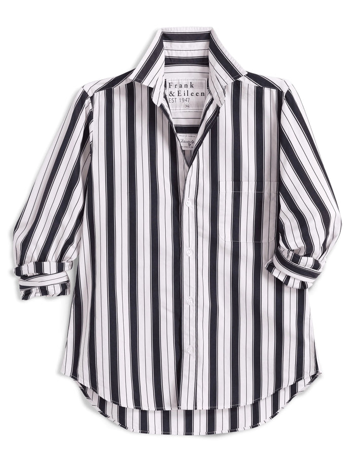 A woman stands outdoors in the sunlight, wearing the FRANK & EILEEN Waverly NYC Button Up Shirt in Italian Brushed Superluxe Cotton with black and tan stripes. The shirt features rolled-up sleeves, and she is buttoning or unbuttoning its perfectly tailored fit.