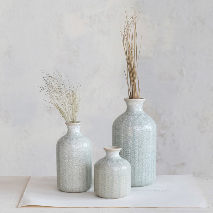 The CREATIVE COOP GRAY EMBOSSED STONEWARE VASE, MEDIUM features a tall, cylindrical shape with a narrow neck, flared rim, and textured leaf-like pattern—ideal as a decorative farmhouse accent.