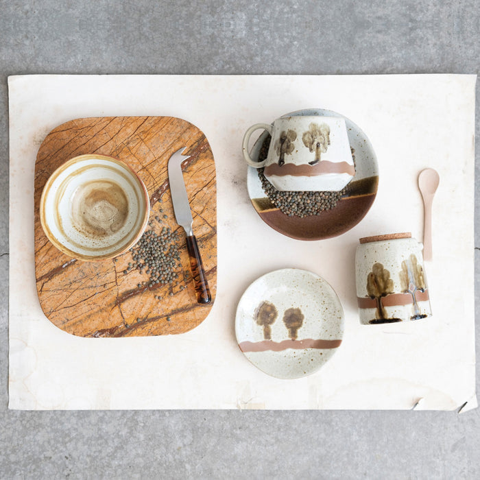 The CREATIVE COOP Hand-Painted Stoneware Jar features a green tree design, cork lid, and wood spoon. Perfect for kitchen storage. Measures 4.25" tall x 3.25" wide.