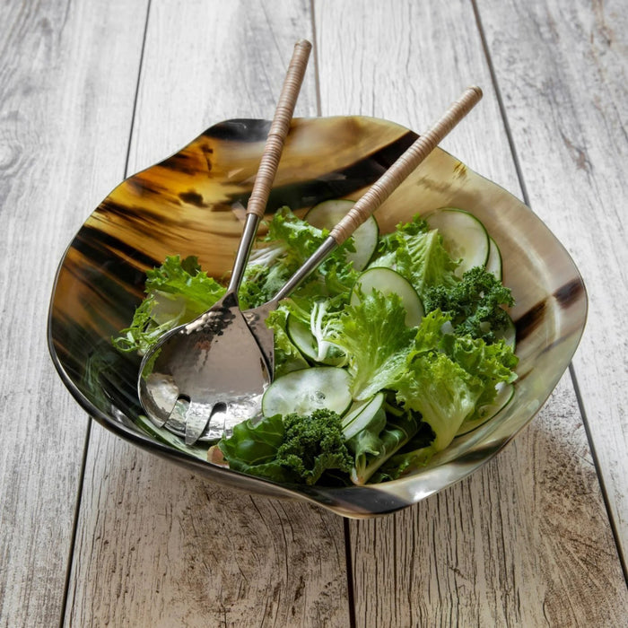 The HORN WAVY ROUND BOWL by BE HOME, INC is an ethically handmade, irregularly shaped bowl crafted from dark marbled horn in Vietnam. It features smooth edges and a natural glossy finish, shown resting on a light blue surface against a blue background.