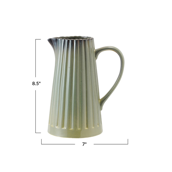 The CREATIVE COOP SAGE GREEN STONEWARE RIBBED PITCHER features a fluted vertical pattern, curved handle, small spout, and smooth reactive glaze, shown against a plain white background.