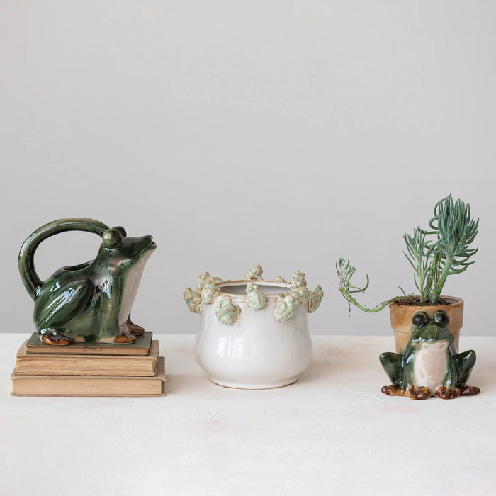 The CREATIVE COOP STONEWARE FROG WATERING PITCHER features a glossy dark green frog shape with brown-accented feet, an arched handle over its back, and a spout at the mouth—ideal as a decorative plant pitcher.