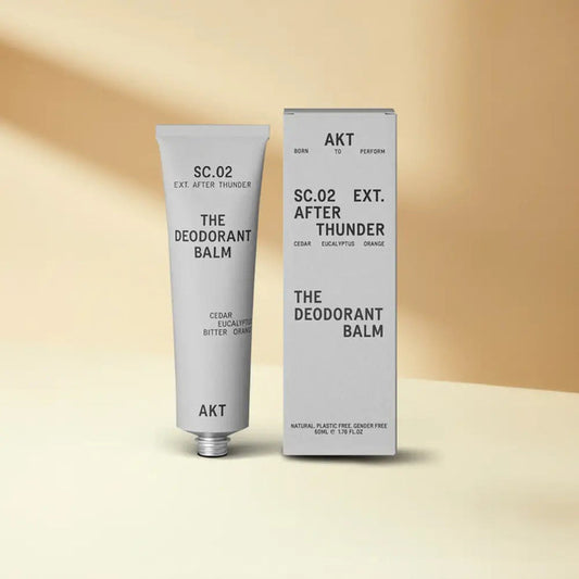 A silver tube of AKT LONDON - DEODORANT BALM AFTER THUNDER (ALUMINUM FREE) stands beside its box, both with minimalist black text on a neutral beige background.
