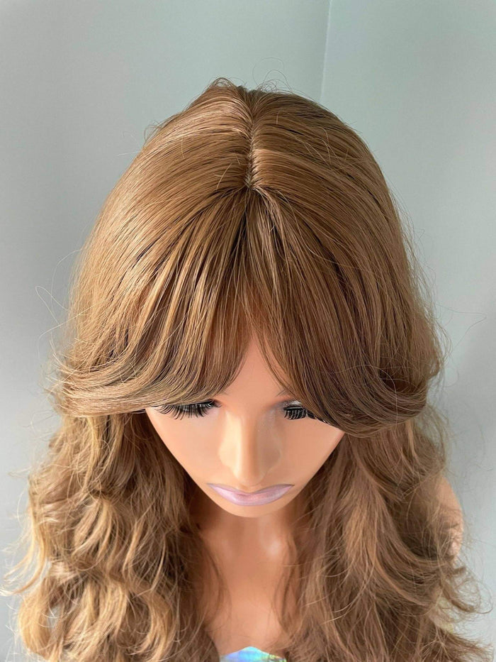 Andrea long brown curly wig with fringe displayed, featuring soft curls and modern curtain bangs.