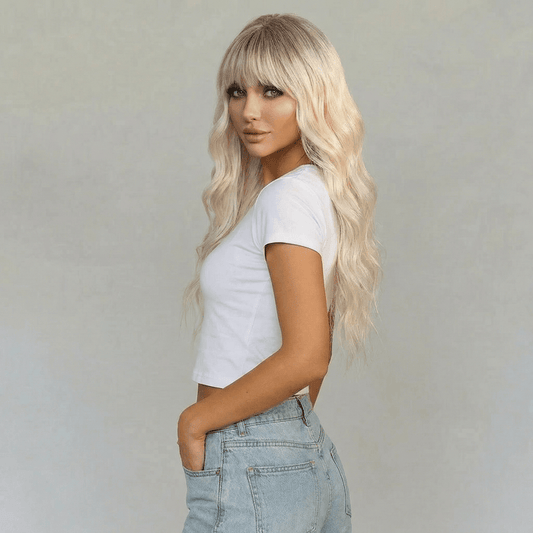 Blaire Ash Blonde Beach Wave Synthetic Wig with Bangs styled on a model in a white crop top and jeans.