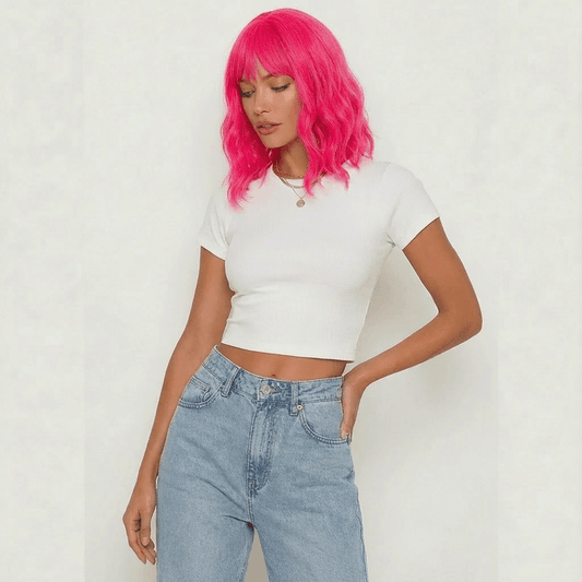 Woman wearing a cerise short neon pink wig with bangs, styled in loose waves, paired with a white crop top.