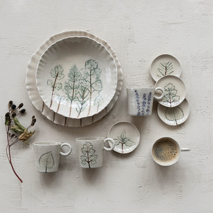 Two views of the CREATIVE COOP HAND-PAINTED ORGANIC SHAPED STONEWARE LOW BOWL WITH BOTANICALS: one features botanical artwork of trees inside, while the other shows its scalloped, organic-shaped edge.