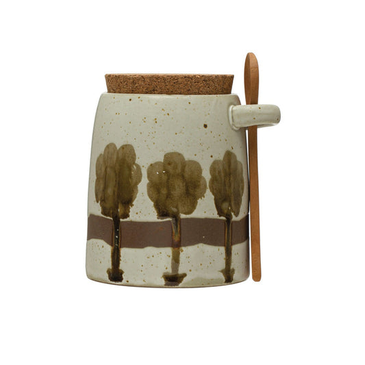 The CREATIVE COOP Hand-Painted Stoneware Jar features a green tree design, cork lid, and wood spoon. Perfect for kitchen storage. Measures 4.25" tall x 3.25" wide.