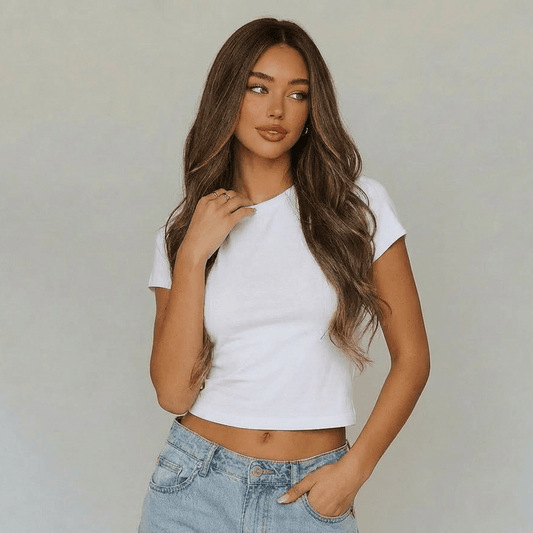 Model wearing a cropped white t-shirt and jeans with long highlighted brown body wave wig.