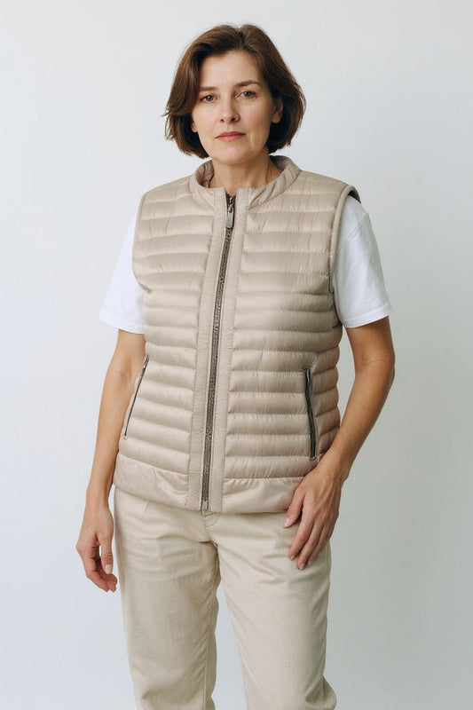 A woman with short brown hair wears the SAVE THE DUCK MARA PUFFER VEST over a white t-shirt and beige pants, standing against a plain light background and looking at the camera with a neutral expression.