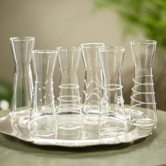Six ZODAX ZALLI SINGLE SERVE GLASS CARAFES are displayed side by side, each showcasing a unique clear raised glass design—lines, waves, dots, and swirls—set against a plain white background.